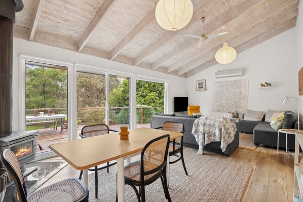 A modern living room with a fireplace, dining area, and a large window offering a view of the outdoors.