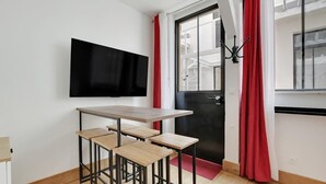 Habitació moderna amb una taula de fusta i quatre cadires, un televisor de pantalla plana muntat a la paret, una porta negra i cortines vermelles.