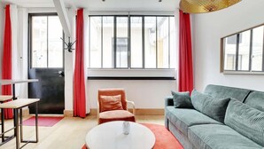 Un saló modern amb un sofà, una cadira, una taula de centre i una finestra gran amb cortines.
