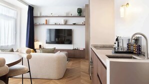 Un salon moderne comprenant un canapé, un téléviseur et un coin cuisine avec un évier et une machine à café.