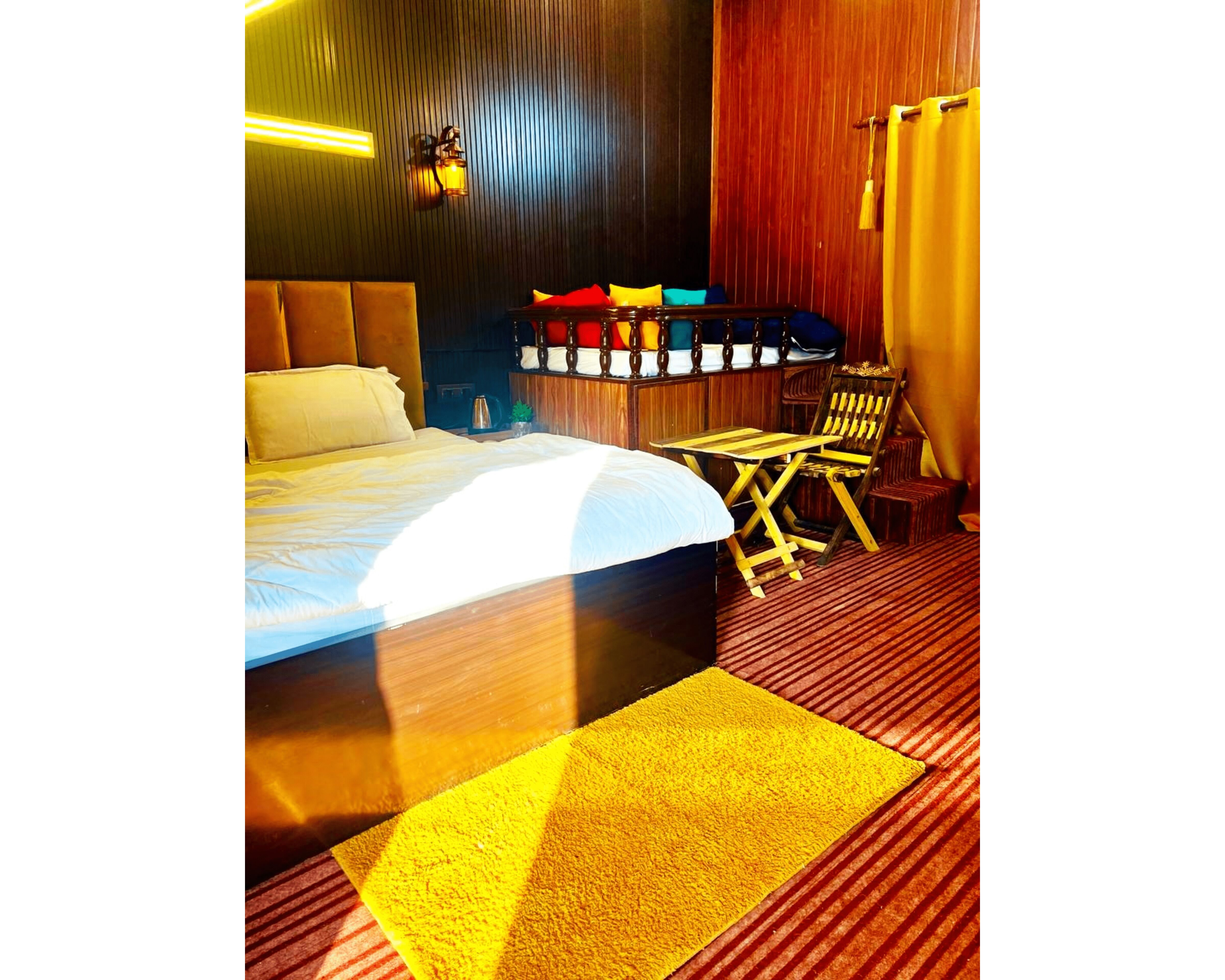 A hotel room with a large bed, a wooden headboard, a small table, a chair, and a yellow rug.