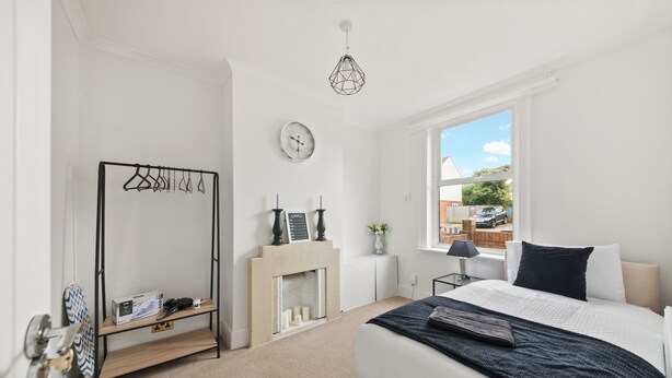 A bedroom with a bed, a bedside table, a hanging light fixture, a coat rack, and a fireplace. - Reading Retreat Spacious 5 Bedroom House (Reading)