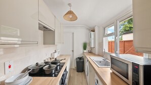 A modern kitchen with white cabinets, a wooden countertop, a stainless steel microwave, and a window providing a view of the outside. - Reading Retreat Spacious 5 Bedroom House (Reading)