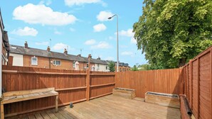 A wooden deck with a bench and a trash bin, surrounded by a wooden fence, with houses and a street lamp in the background. - Reading Retreat Spacious 5 Bedroom House (Reading)