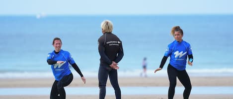 Three people in wetsuits on a beach with surfboards.