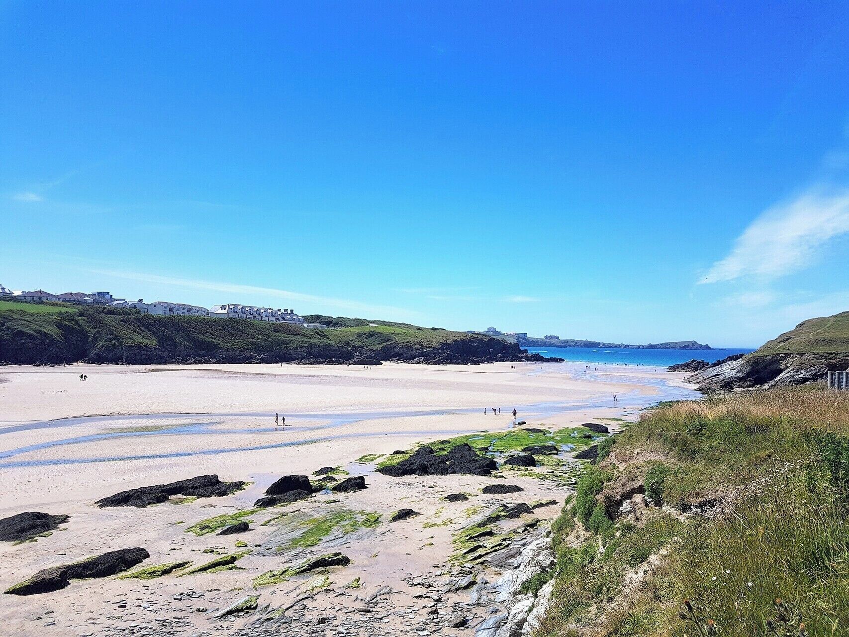 A coastal beach with a sandy shore, rocky outcrops, and grassy hills.