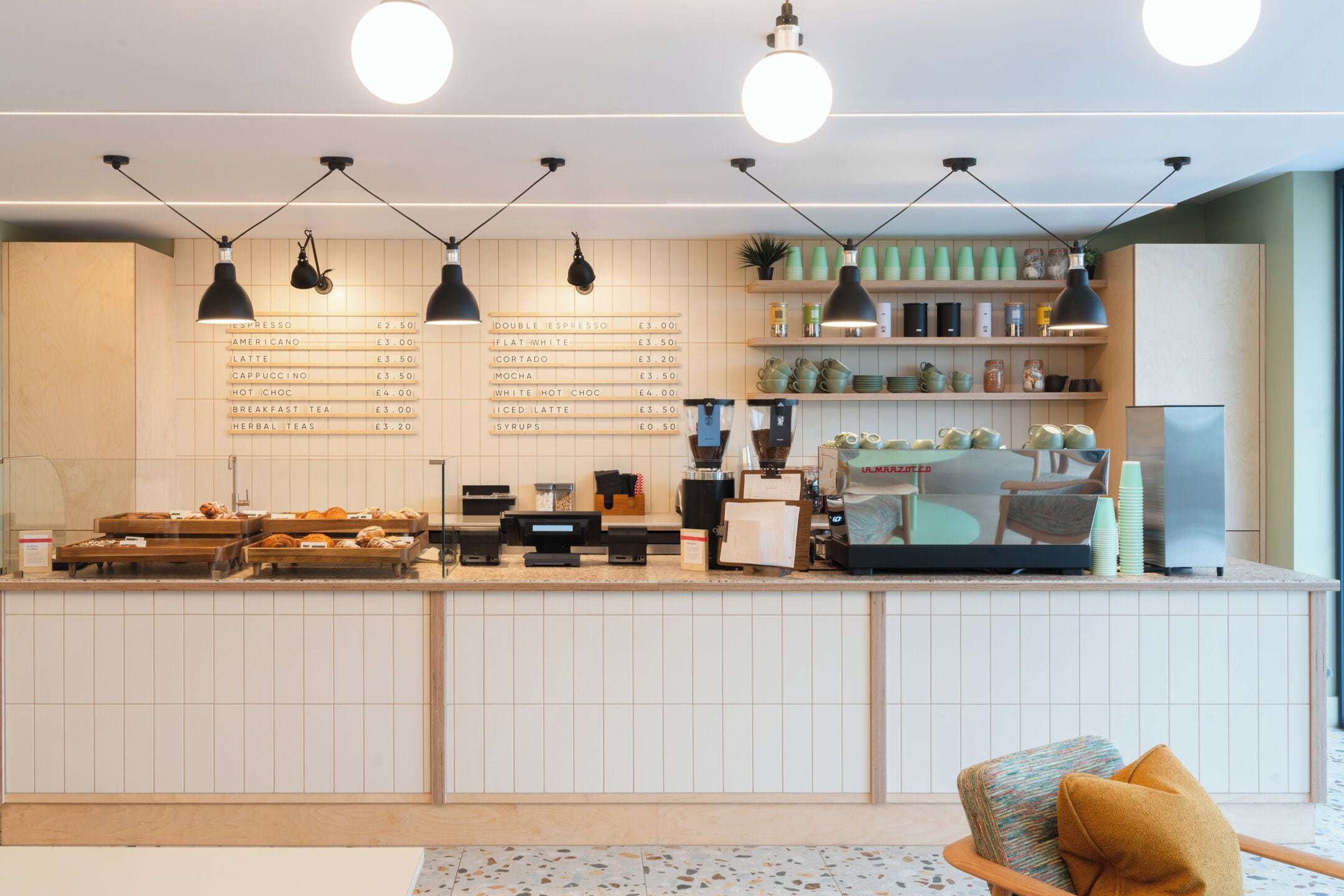 Un café moderne doté d’un tableau affichant le menu, de machines à expresso et d’une variété de tasses à café exposées.