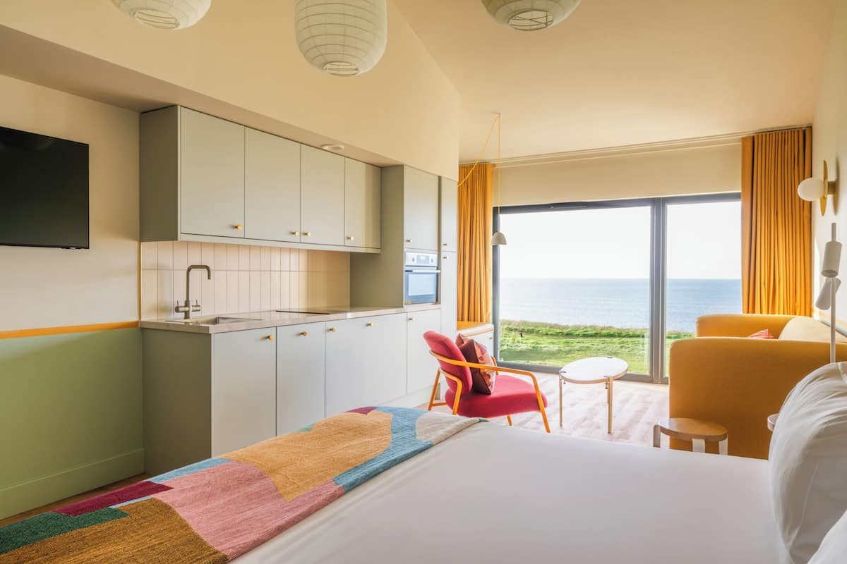 Une chambre d’hôtel avec un lit, un petit bureau, une chaise, une télévision et une vue sur la mer.