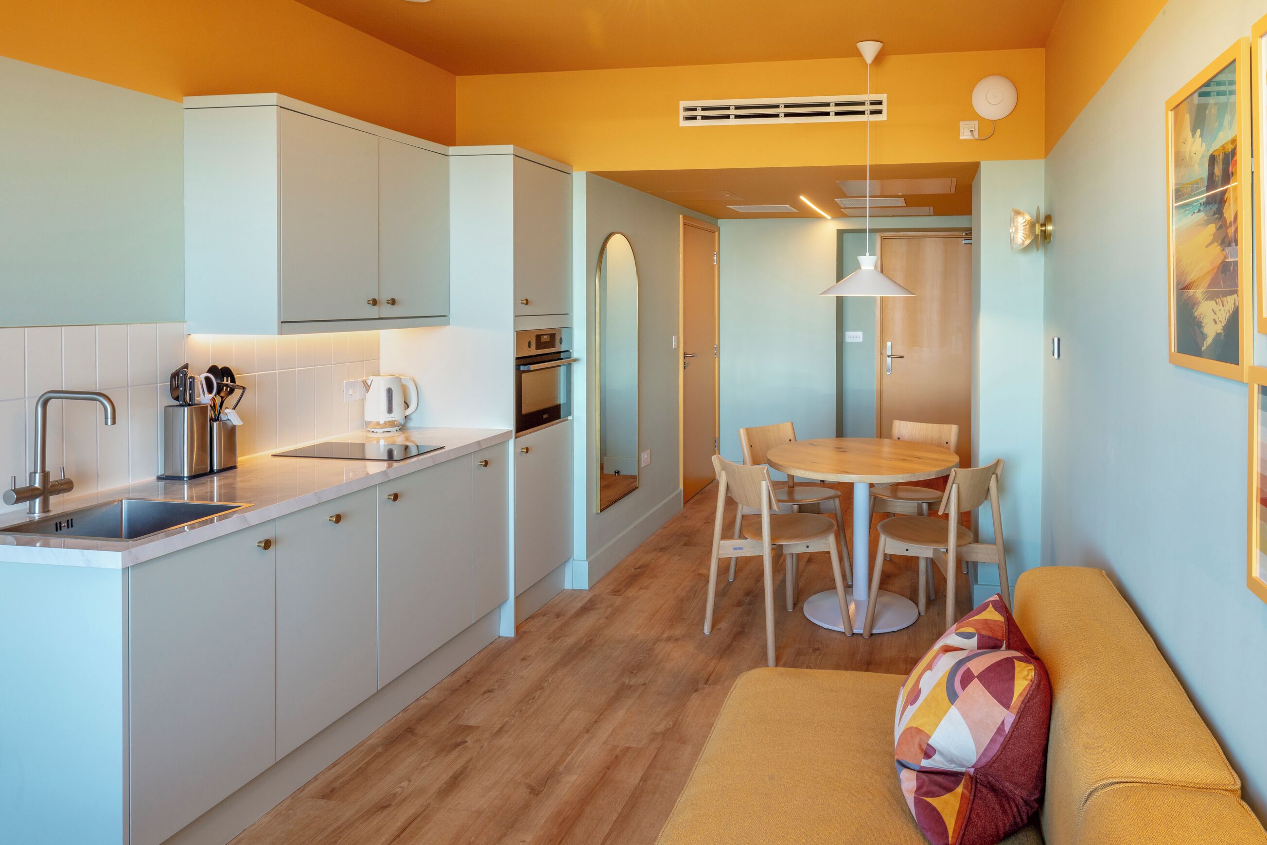 Una cocina compacta con armarios blancos, un lavamanos y un comedor con mesa y sillas.
