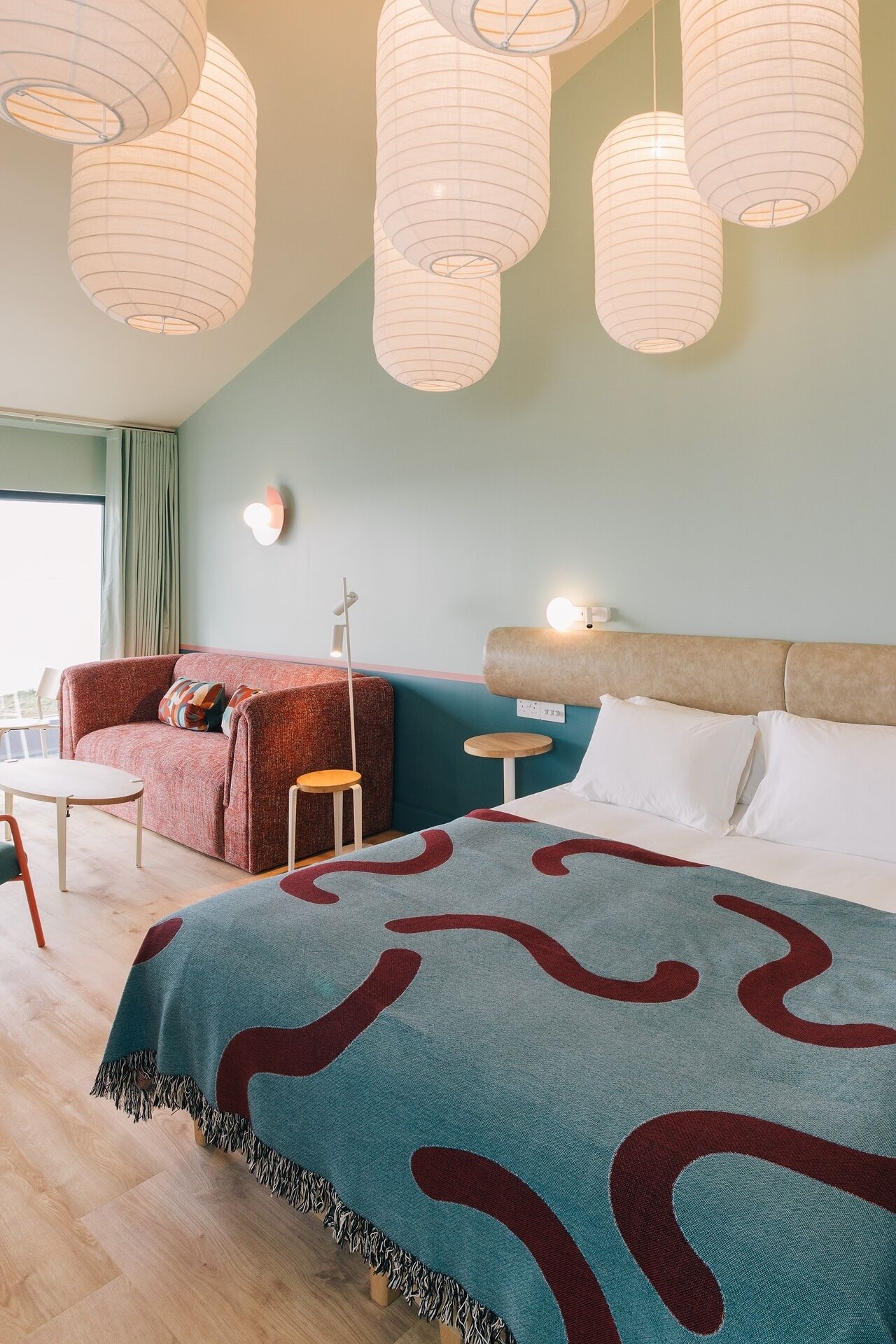 A modern bedroom with a large bed, a red sofa, a small table, and hanging paper lanterns.