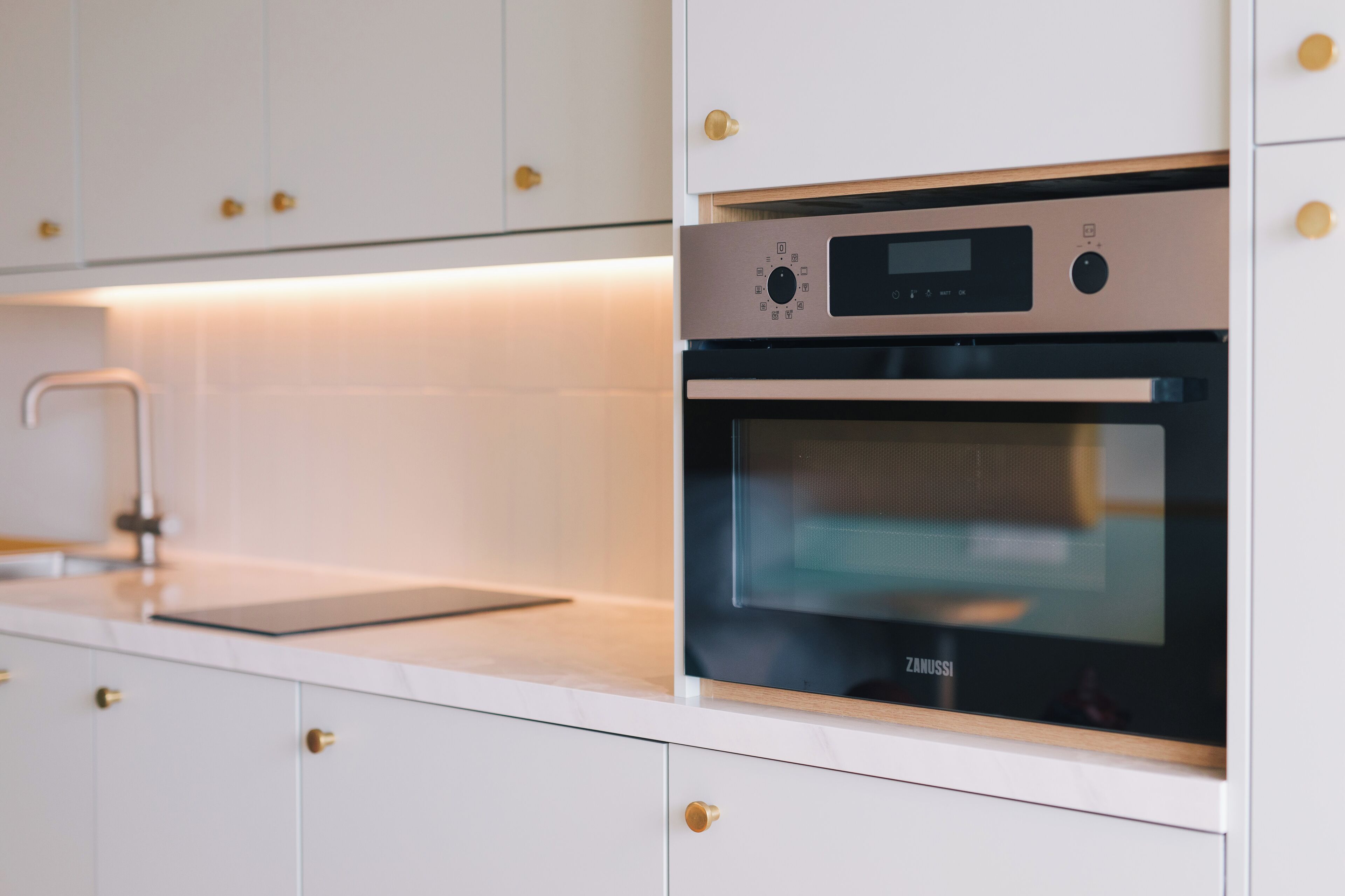 A modern kitchen with white cabinetry, a built-in oven, and a stainless steel range hood.