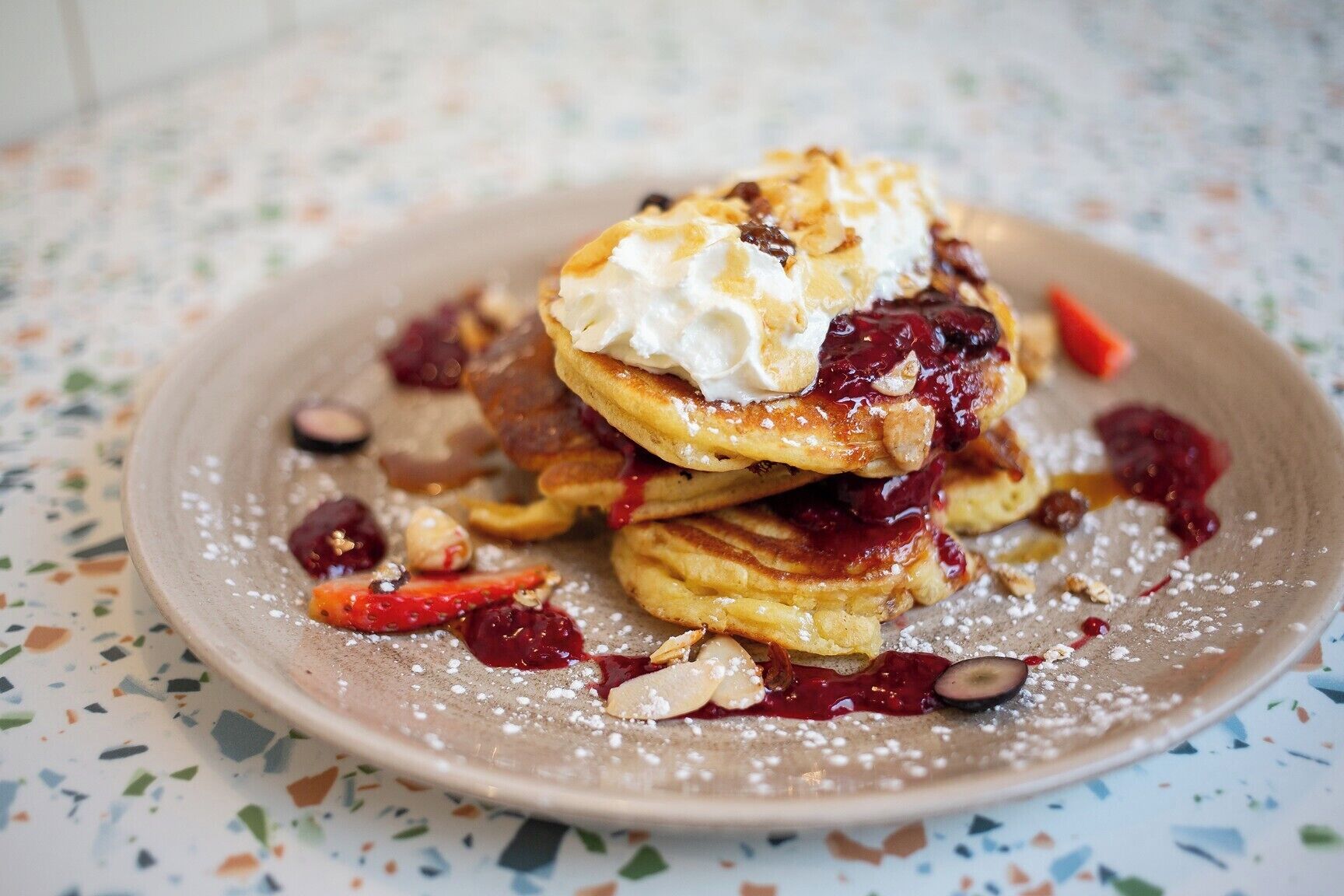 A stack of pancakes with whipped cream and berries on a speckled plate.