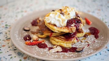 A stack of pancakes with whipped cream and berries on a speckled plate.
