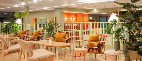 A modern lounge area with wooden furniture, colorful cushions, and potted plants.