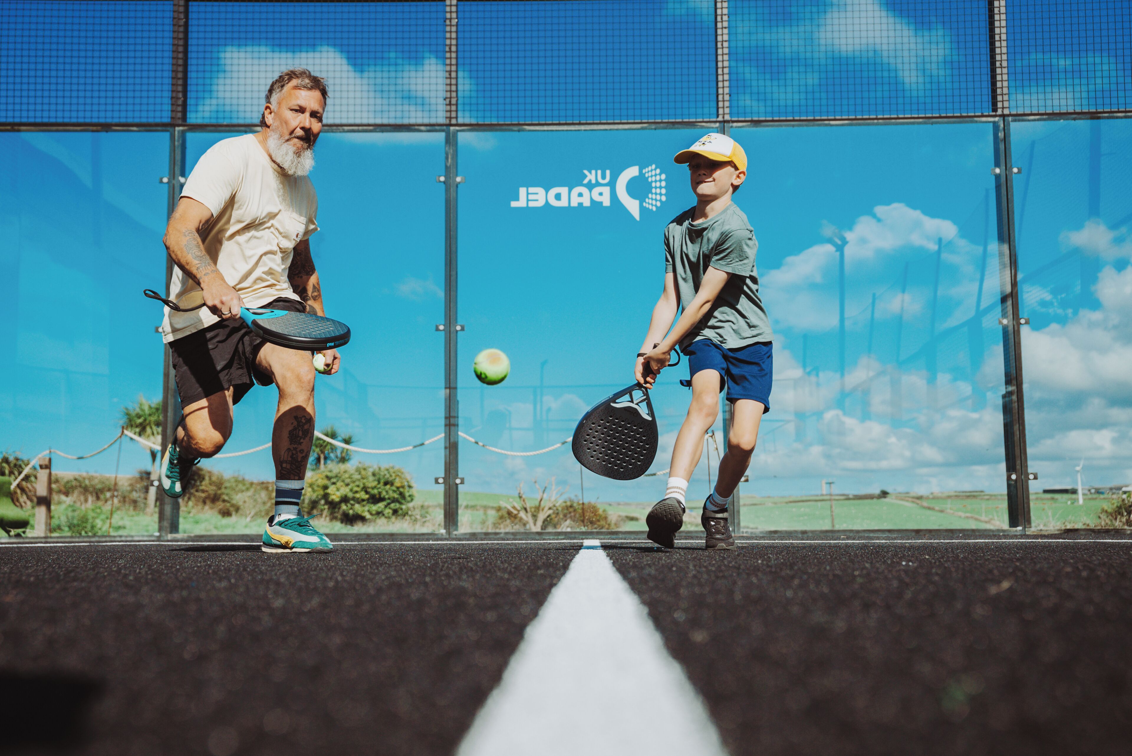 Two people playing tennis on an outdoor court with a clear sky in the background.