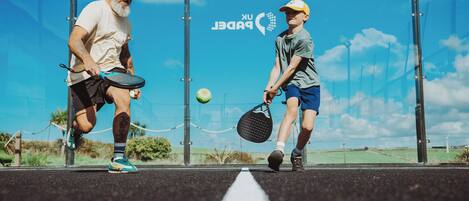 Two people playing tennis on an outdoor court with a clear sky in the background.