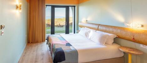 A hotel room with a large bed, a bedside table, a window with curtains, and a view of the outdoors.