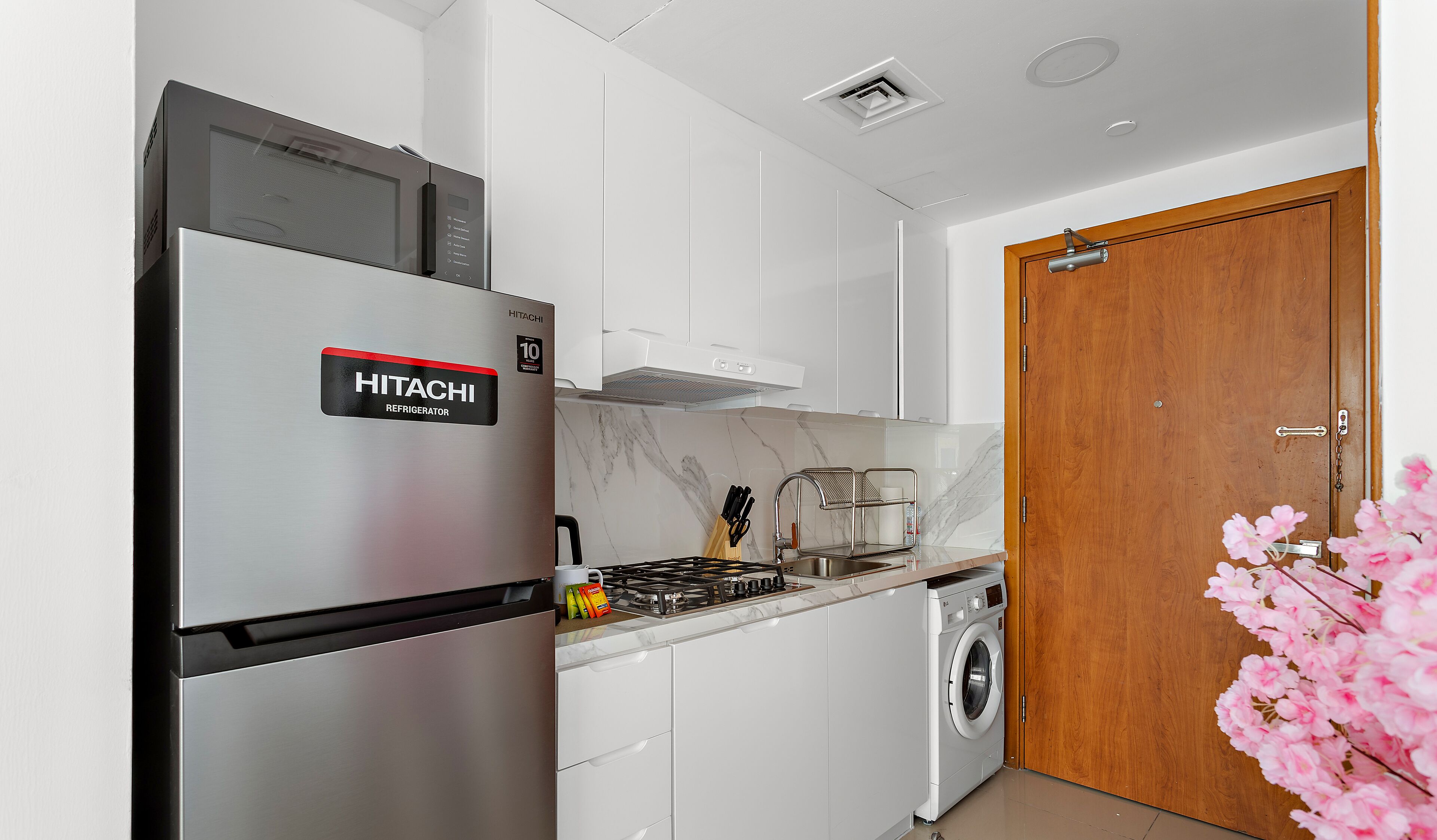A modern kitchen with a stainless steel refrigerator, a built-in oven, a washing machine, and a wooden door.