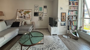 A living room with a sofa, a coffee table, a bookshelf, and a world map on the wall. - Modern 2BD Flat in Mile End with Private Balcony (Greater London)