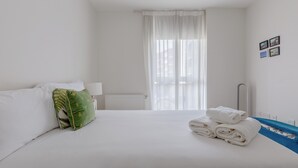 A hotel room with a neatly made bed, a radiator, a window with sheer curtains, and a wall with a few pictures. - Modern 2BD Flat in Mile End with Private Balcony (Greater London)