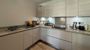 A modern kitchen with light wood cabinets, a stainless steel sink, and a black induction cooktop. - Modern 2BD Flat in Mile End with Private Balcony (Greater London)