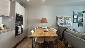 A compact kitchen with modern appliances, a wooden dining table, and a cozy seating area. - Modern 2BD Flat in Mile End with Private Balcony (Greater London)