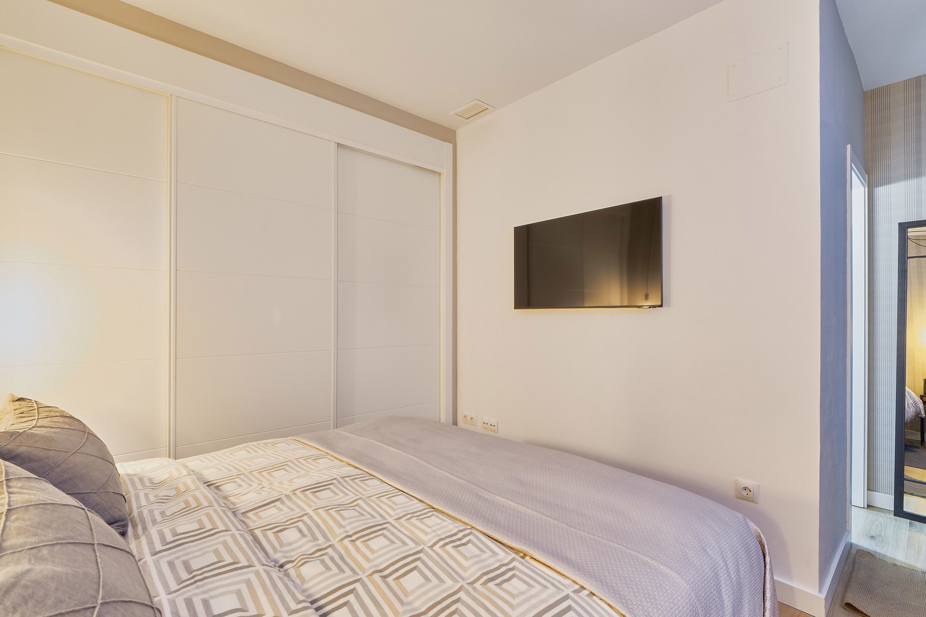 Ein Schlafzimmer mit einem Bett, einem Kleiderschrank und einem an der Wand befestigten Fernseher.