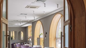 Egy modern belsőépítészeti megoldásokkal rendelkező étterem, melynek jellemzői a faívű oszlopok, a lila színű ülőhelyek és a csempézett padló.