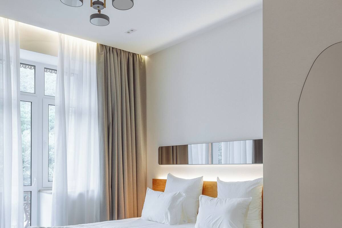 Quarto de hotel moderno com uma cama grande, cabeceira de madeira e luminária no teto.