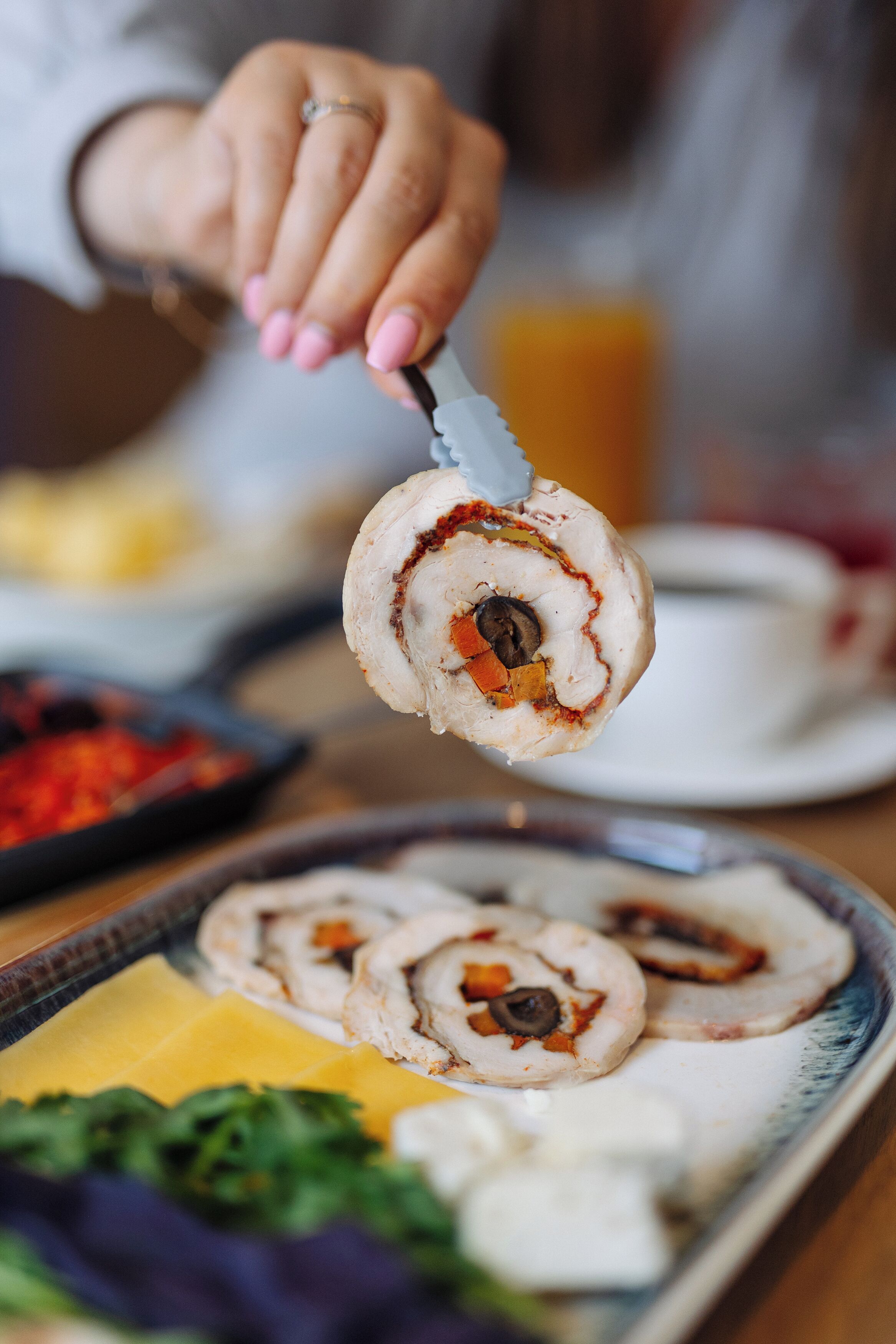 A person holding a rolled pastry with a filling, on a tray with other food items.