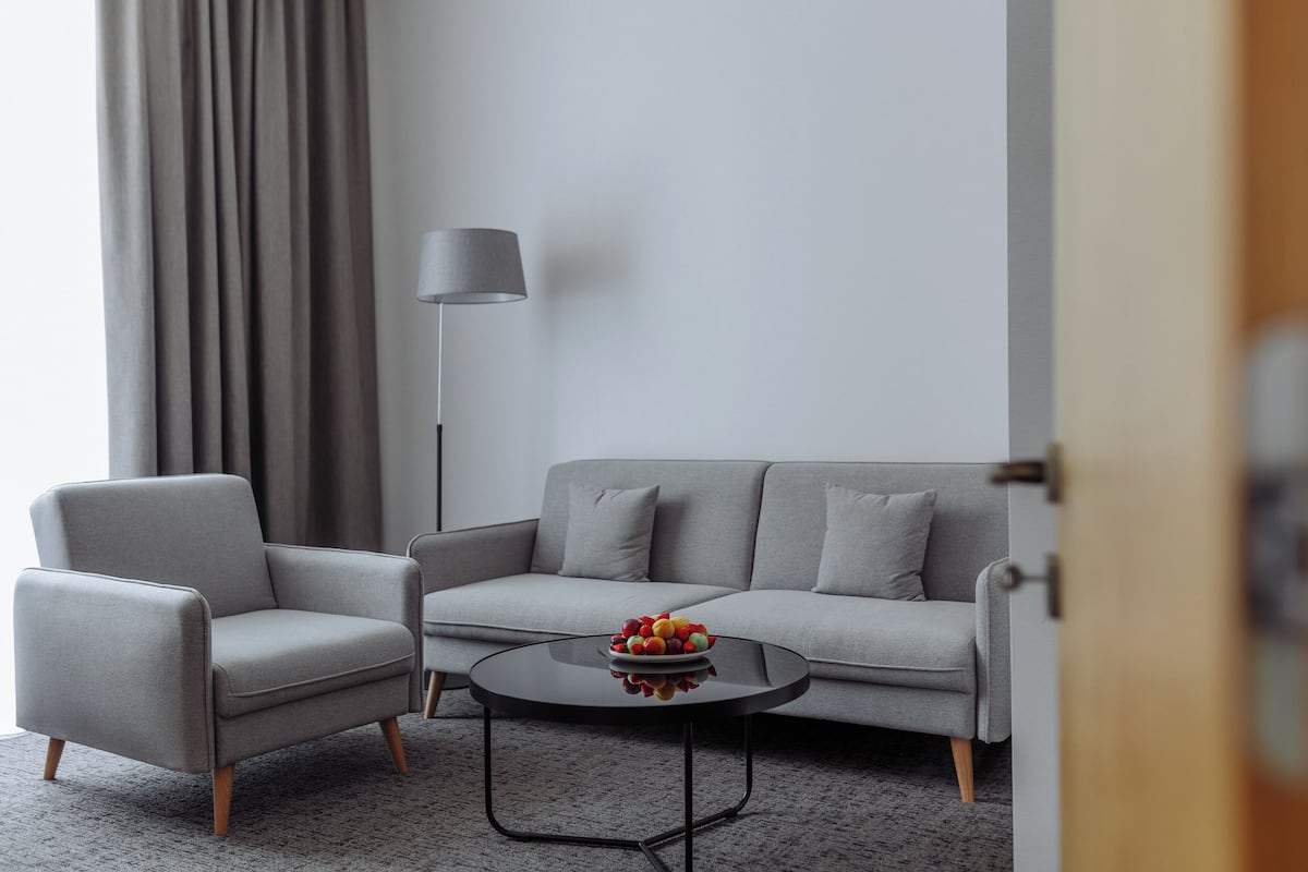 Uma sala de estar moderna com um sofá cinzento, uma poltrona cinza e uma mesa de centro redonda com uma fruteira.