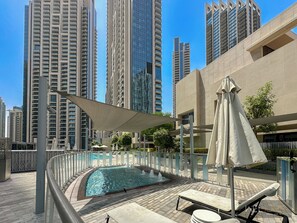 A rooftop swimming pool with lounge chairs and umbrellas, surrounded by high-rise buildings.