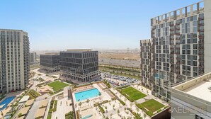 A high-rise residential building with multiple balconies, a central courtyard with a swimming pool, and a parking area. - WelHome - Beautiful 1BR Apt in Dubai Hills with City View (Dubai)