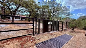 A gated property with a metal fence, a paved driveway, and a building with a red roof. - Costa Rican Private Villa | monkeys visit the trees! (Venado)