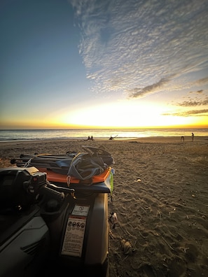 A beach scene with a dune buggy parked on the sand, a clear sky, and the ocean in the background.