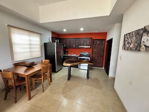 A compact kitchen with a refrigerator, stove, and dining area with chairs and a table.