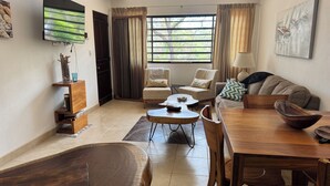 A living room with a dining area, a TV mounted on the wall, a window with curtains, and a painting on the wall. - Costa Rican Private Villa | monkeys visit the trees! (Venado)