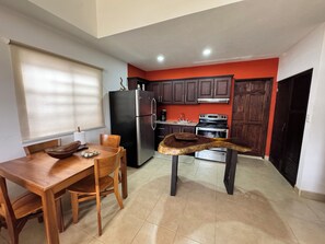 A kitchen with a dining table, chairs, a refrigerator, a stove, and cabinets.