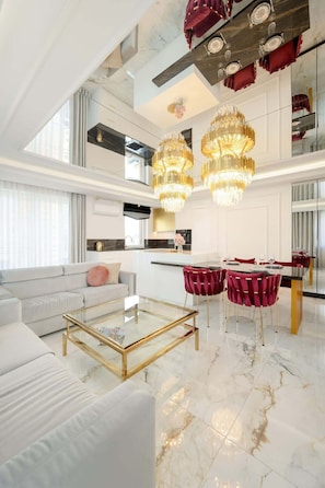 Un intérieur moderne avec un canapé, une table basse en verre, un coin repas avec des chaises rouges et une cuisine en arrière-plan.