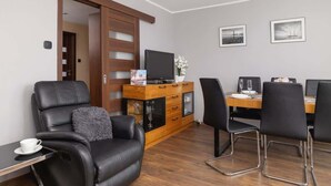 A modern room with a leather chair, a wooden cabinet with a TV, and a dining table with chairs. - Spacious Apartment for 6 Persons | Balcony | 3 Bedrooms (Kraków)