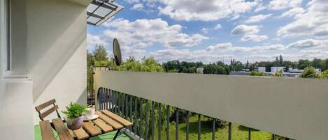 A balcony with a green artificial grass floor, wooden furniture, and a metal railing.
