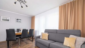 A modern living room with a grey sofa, black chairs, a wooden dining table, and a chandelier. - Spacious Apartment for 6 Persons | Balcony | 3 Bedrooms (Kraków)