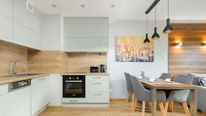 Une cuisine moderne avec des meubles blancs, un four encastré et un coin repas comprenant une table en bois et des chaises grises.