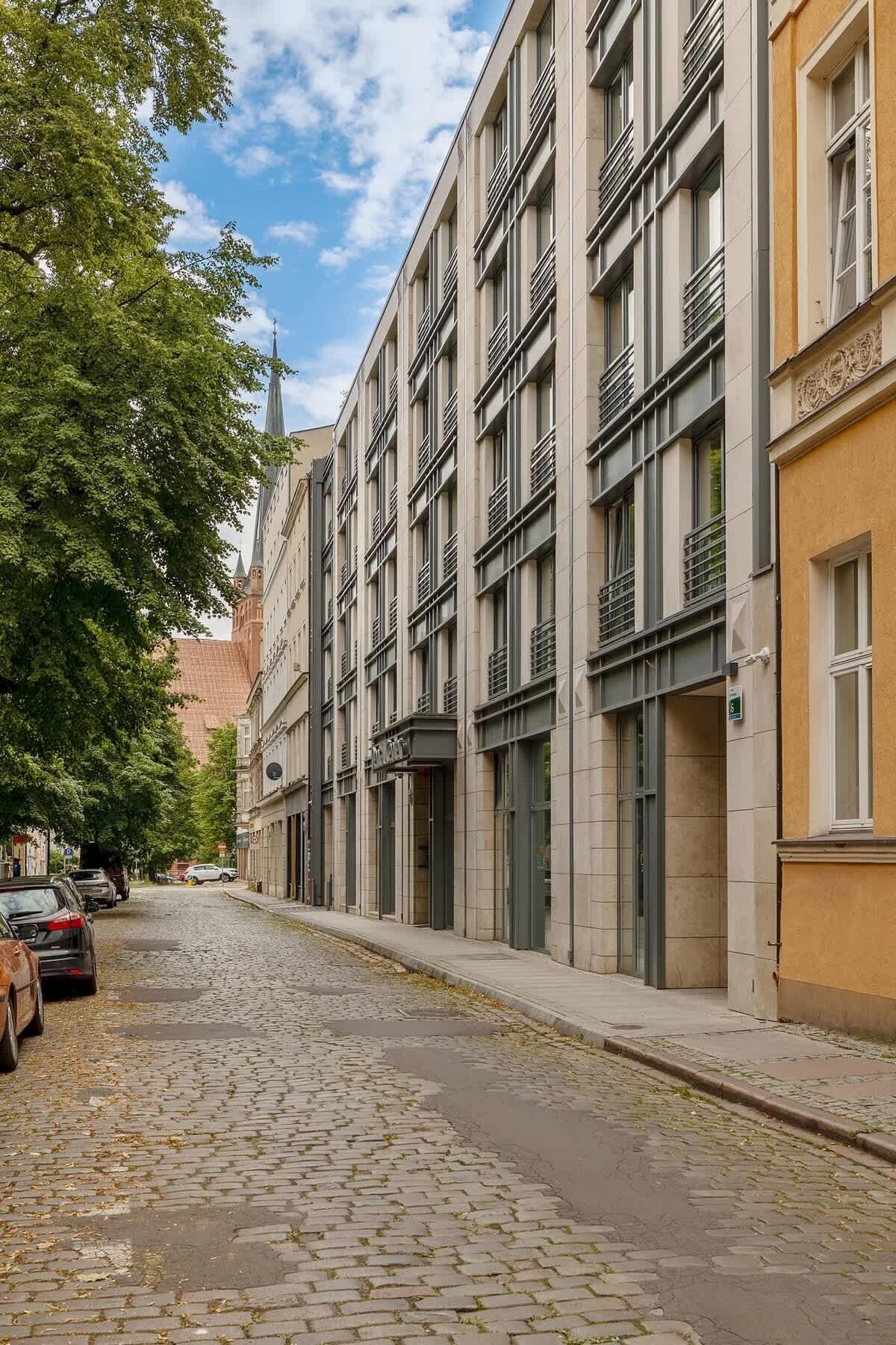 Una strada con lastricato in pietra, edifici a più piani con ampie vetrate e automobili parcheggiate.
