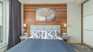 Une chambre d’hôtel moderne avec un grand lit, un mur décoratif en bois et un tableau représentant un arbre.