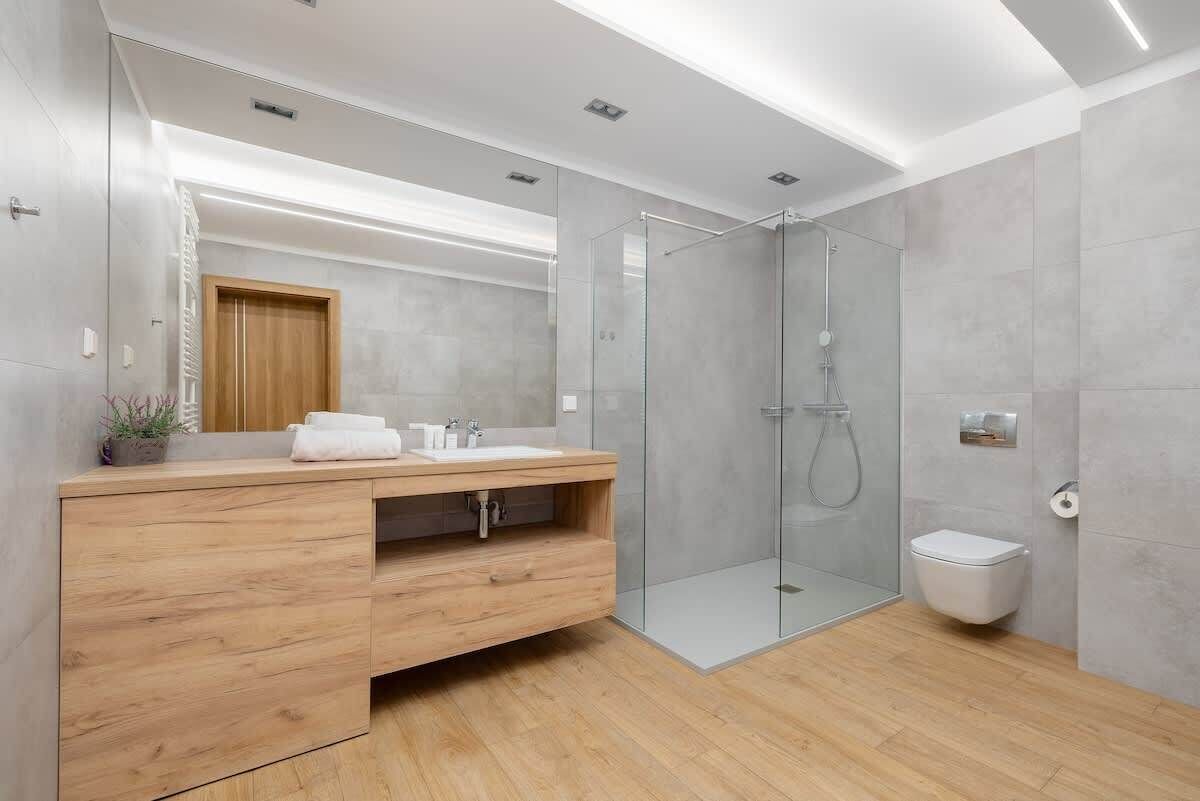A modern bathroom with a wooden vanity, a glass shower enclosure, and a toilet.