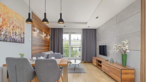 Un salon moderne comprenant un coin repas, de grandes fenêtres, un téléviseur à écran plat et un meuble en bois.