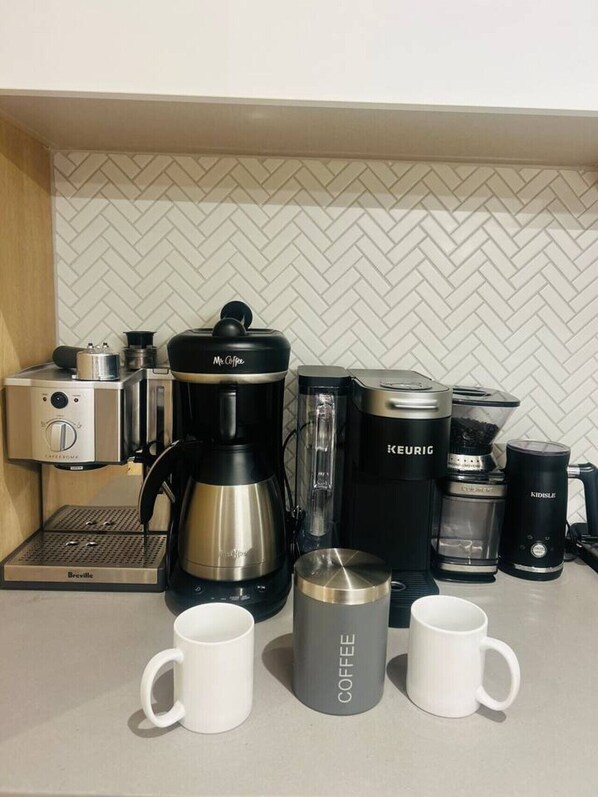 Una kitchenette con cafetera, hervidor, molinillo de café y dos tazas blancas.