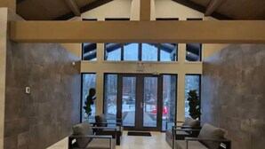 A spacious lobby with a high ceiling, large windows, and a stone wall.