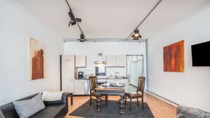 Una sala de estar moderna con un sofá, una mesa de comedor con sillas, una cocina al fondo y obras de arte en las paredes.